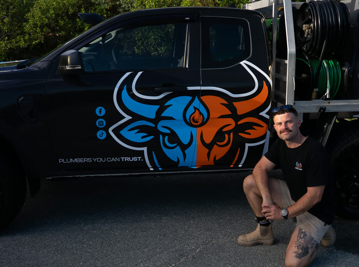Joel kneeling beside the Oxplumb ute with the bull logo