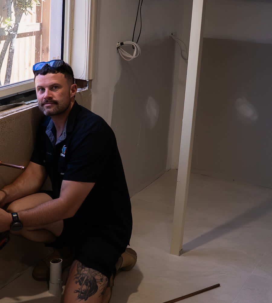 Joel at exposed pipes in a bathroom wall